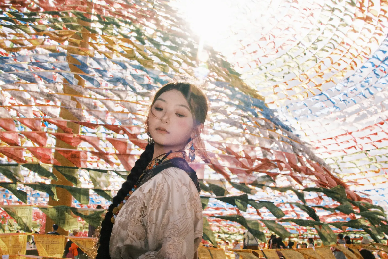 女子站在经幡下仰头，逆光穿过彩旗