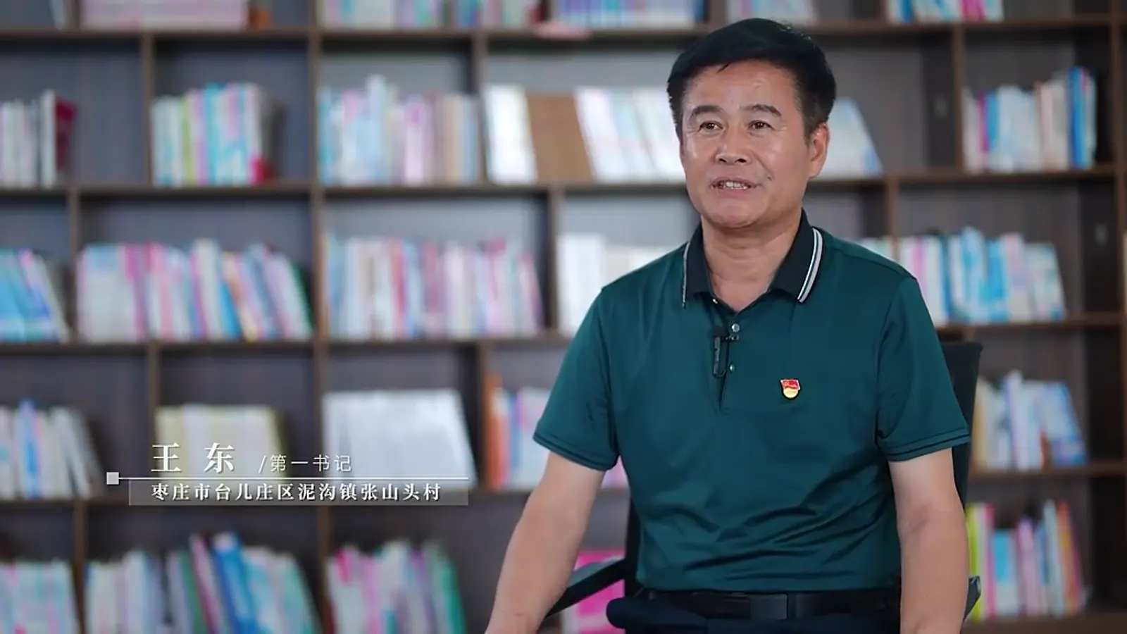 受访者坐在书架前，画面左下角是人物姓名条